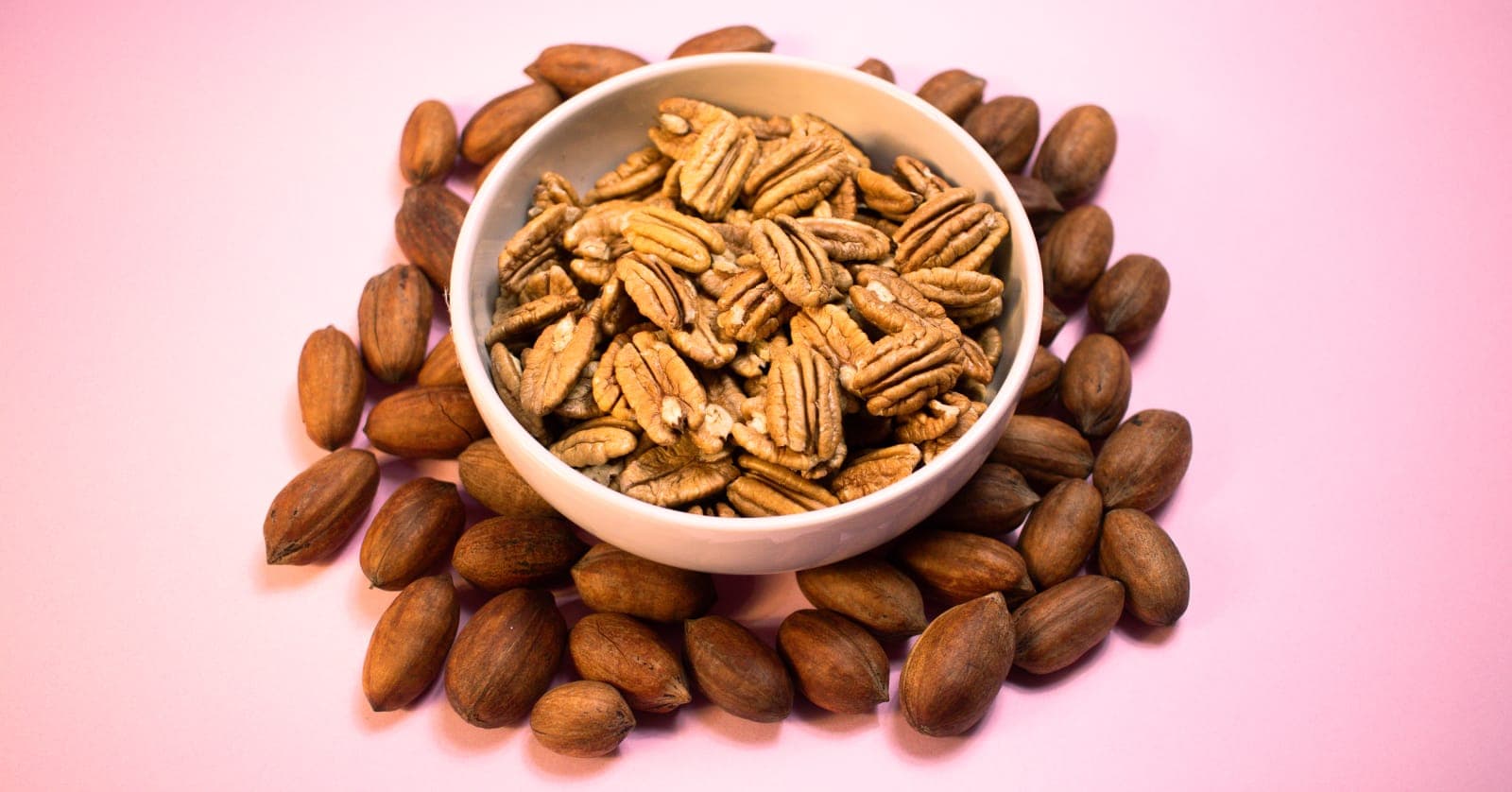 Tazón de nueces pecanas peladas rodeado de nueces con cáscara